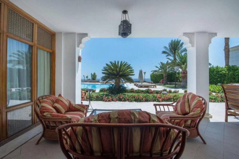 Eine überdachte Terrasse mit Rattanmöbeln, mit Blick auf den blühenden Garten, einen Pool und das Meer