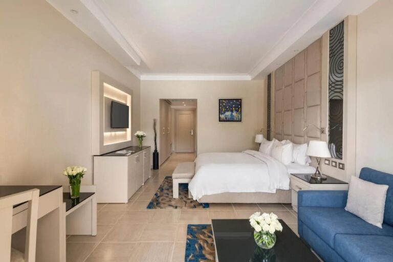 Ein Zimmer mit Doppelbett, blauem Sofa und Wandfernseher