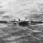 Schwarz-Weiß-Archivfoto aus einem Flugzeug: Ein U-Boot fährt an der Oberfläche über ein gekräuseltes Meer, mit Kielwasser am Rumpf und dem Turm in der Mitte.