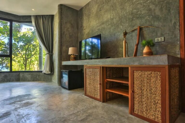 Ein Fernseher auf einem Möbel aus Holz und Rattan, neben einer Minibar und einer Glasfront