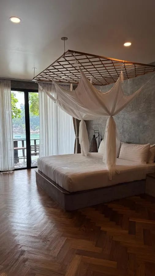 Ein Zimmer mit Fischgrätparkett, einem Bett unter Moskitonetz und einer Glastür zum Meer