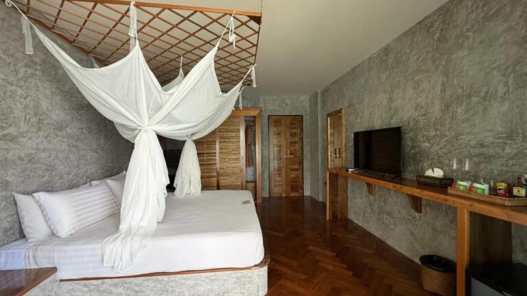 Ein Zimmer mit Fischgrätparkett, einem Bett unter Moskitonetz, Fernseher und Tee-Ecke