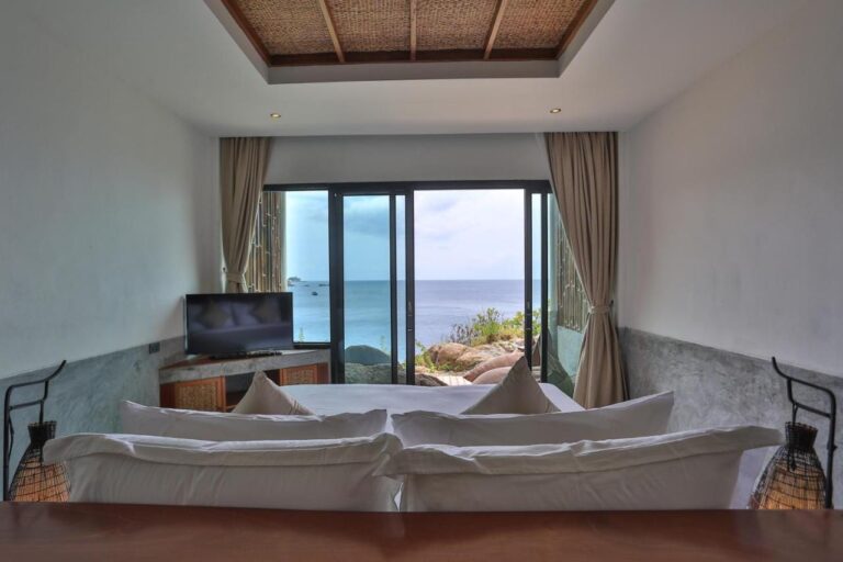 Ein Zimmer mit Meerblick, vom Kopfende des Betts aus gesehen, mit zwei Korblampen