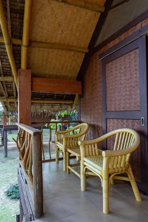 Eine geflieste Veranda mit zwei Rattansesseln vor einer geflochtenen Wand