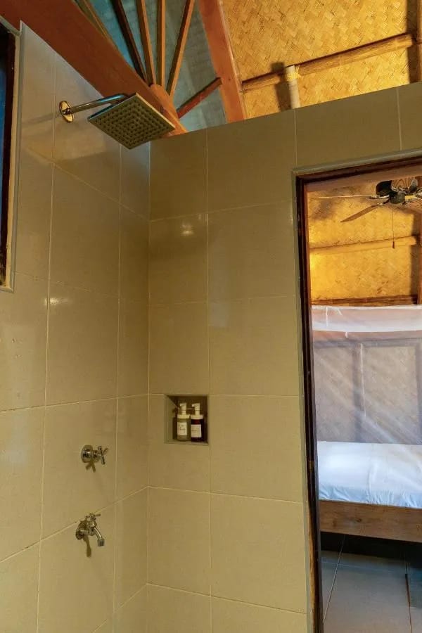 Eine geflieste Dusche, offen zum Zimmer mit seinem Bett unter Moskitonetz