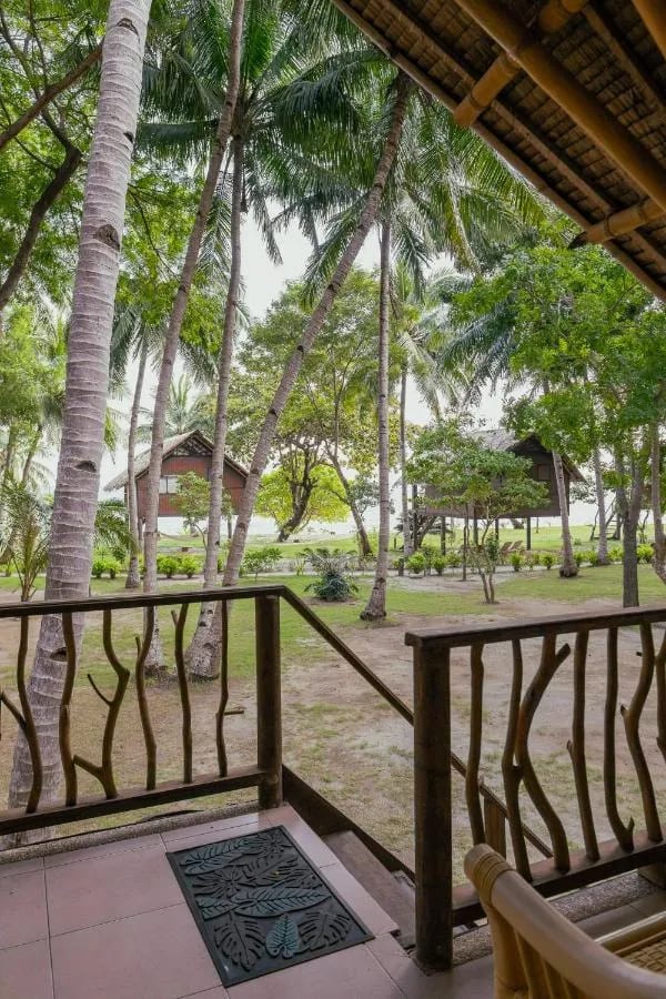 Blick von einer Veranda auf Palmen, Rasen und Bungalows auf Stelzen