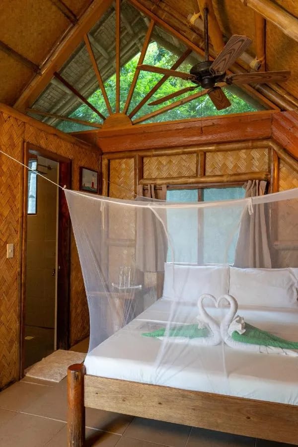 Ein Bett unter Moskitonetz mit zwei Handtuchschwänen, im Hintergrund das Bad