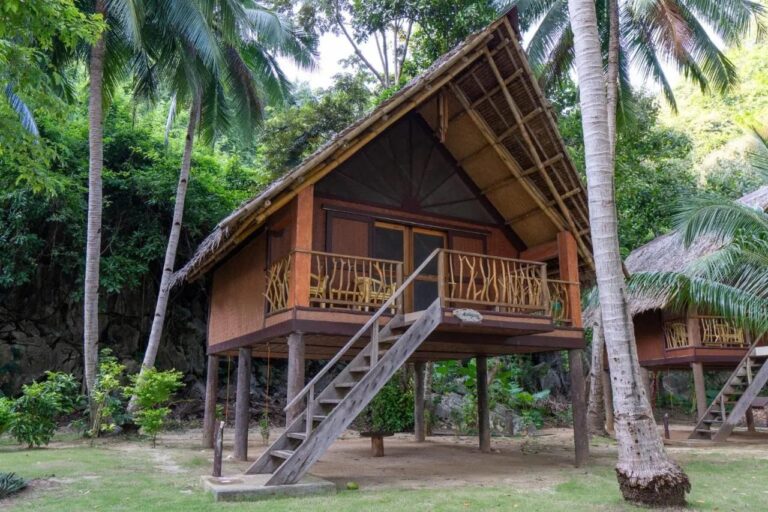 Ein Stelzenbungalow des Sangat Island Dive Resorts mit Holztreppe, unter Palmen