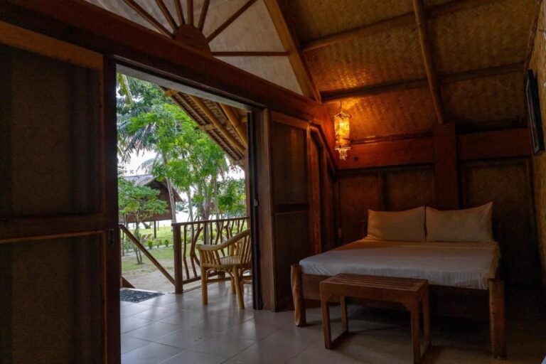 Ein Zimmer mit Doppelbett, offen zur Veranda, mit Rattansessel und Garten