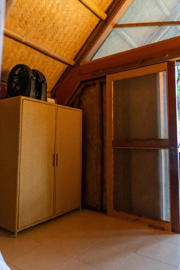 Ein geflochtener Schrank mit zwei Ventilatoren darauf, neben einer Tür mit Moskitogitter