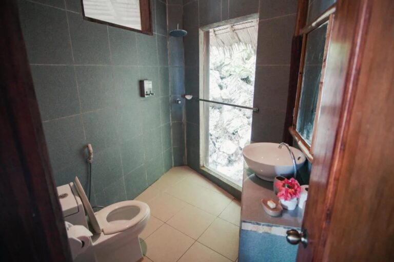 Ein dunkelgrün gefliestes Bad mit Waschbecken, Dusche und Fenster zu den Felsen