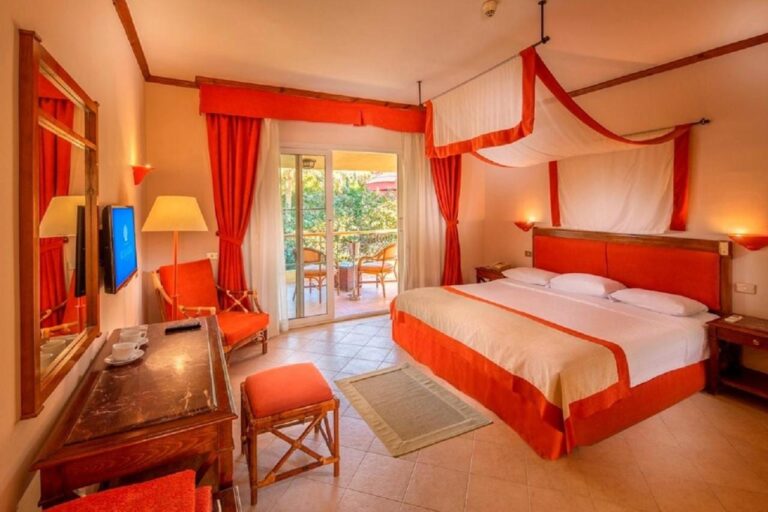 Ein Zimmer mit Doppelbett unter einem weiß-orangen Betthimmel, offen zum Balkon