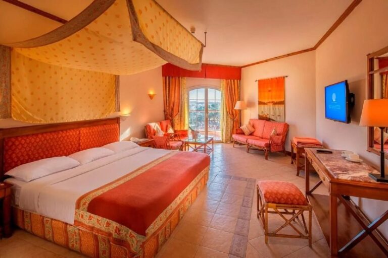 Ein großes Zimmer mit Bett unter einem Betthimmel, einem orangen Sofa und einem Schreibtisch