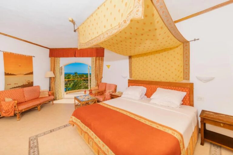 Ein Zimmer des Siva Grand Beach mit Doppelbett unter einem gelben Betthimmel, einer orangen Sitzecke und dem Meer in der Ferne