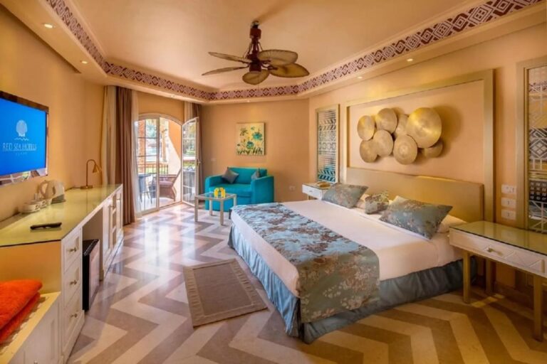 Ein Zimmer mit Doppelbett, Deckenventilator, blauem Sessel und Fischgrätboden