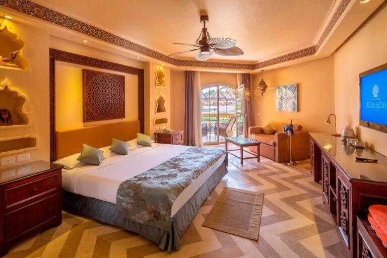 Ein Zimmer mit Doppelbett, beleuchteten Nischen, Deckenventilator und Fenstertür zum Balkon