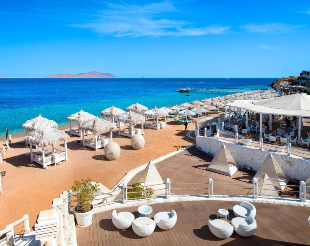 Der Strand des Sunrise Arabian Beach Resorts mit Strohschirmen und Steg, gegenüber der Insel Tiran