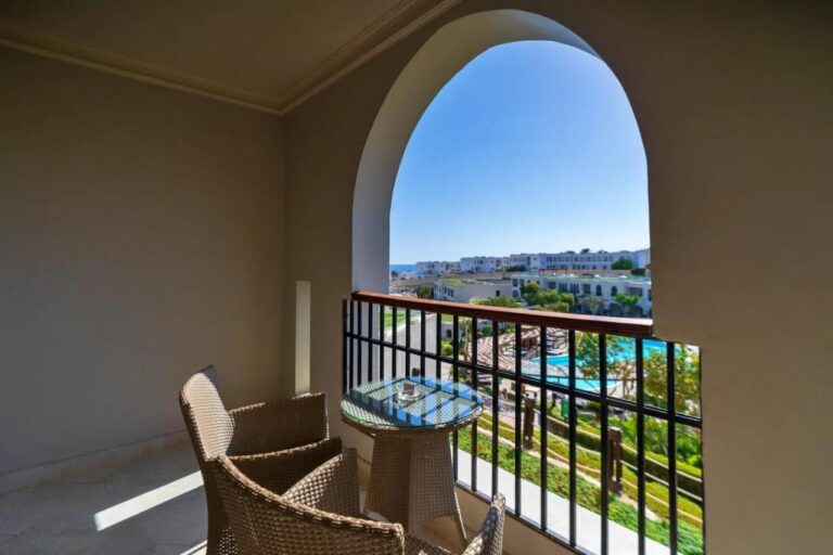 Ein Balkon unter einem Bogen, mit zwei Korbsesseln, über den Pools und Gärten