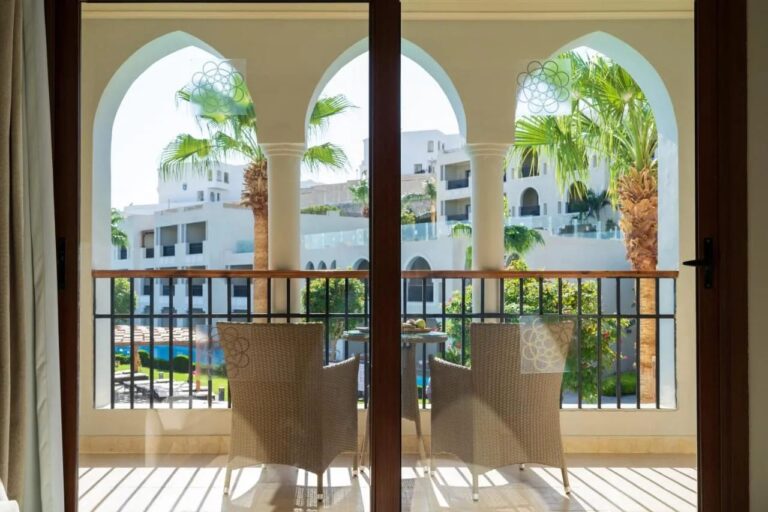 Ein Balkon mit Arkaden und zwei Korbsesseln, mit Blick auf die Palmen und die weißen Gebäude des Sunrise Arabian Beach Resorts