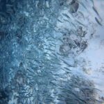 Ein dichter Schwarm silbriger Sardinen streift über einen sehr hellen Sandgrund mit dunklen Felsen, links ist die Masse der Fische am dichtesten, im Blau.