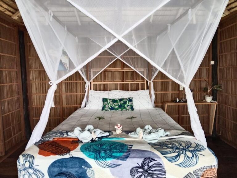 Ein Bett unter Moskitonetz, mit einer Tagesdecke mit blauen Blättern und gefalteten Handtüchern
