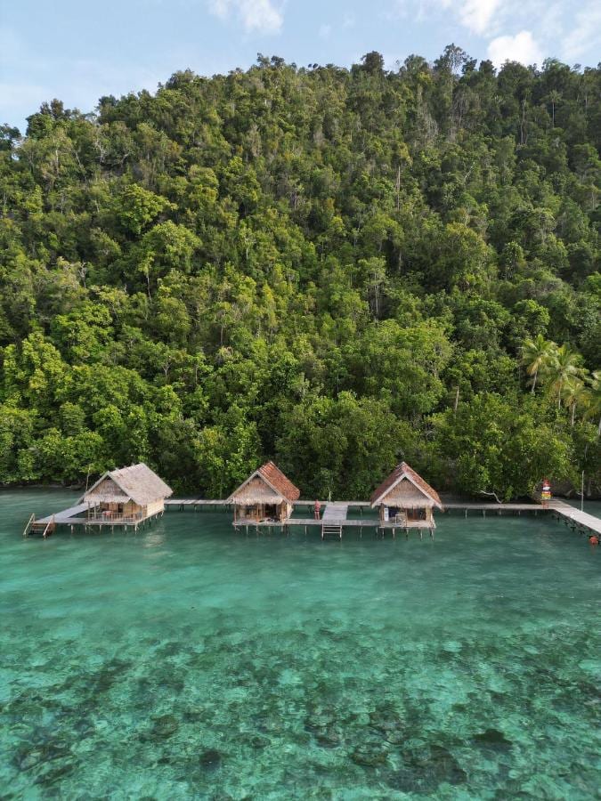 Drei Stelzenbungalows über türkisfarbenem Wasser am Fuß des Waldes