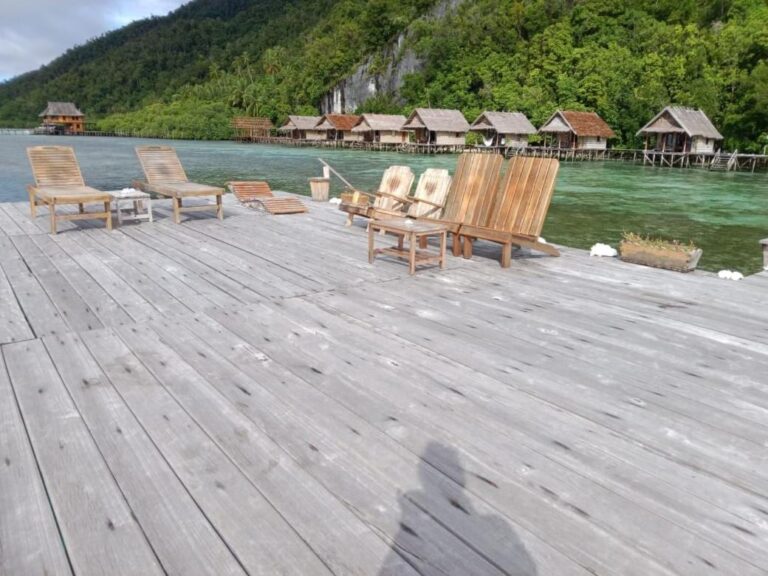 Ein Holzsteg mit Liegestühlen, gegenüber der Reihe der Stelzenbungalows