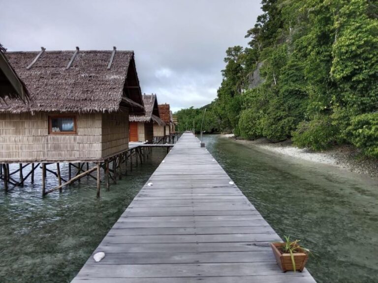 Ein Holzsteg über dem Wasser, entlang der Bungalows mit Palmblattdächern