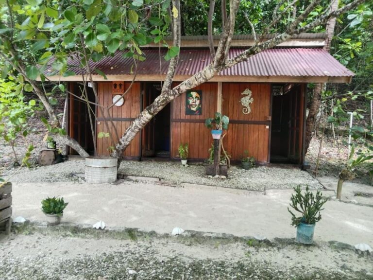 Das Toilettenhäuschen aus Holz unter den Bäumen, mit einem dekorativen Seepferdchen