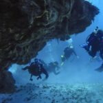 Vier Taucher kommen aus einem Korallentunnel über Sandgrund, auf Cozumel, die Felsdecke über ihnen
