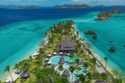 Luftaufnahme des Two Seasons Coron mit Pools und Palmen auf einem schmalen Landstreifen zwischen zwei Stränden