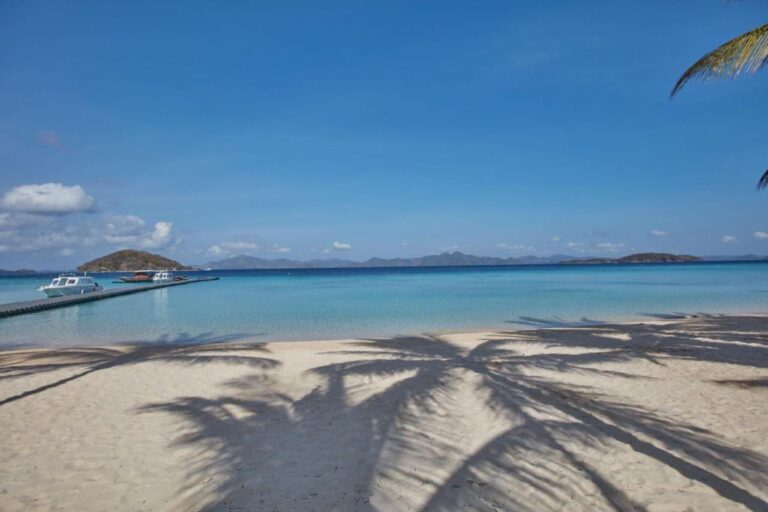 Palmenschatten auf dem Sand, mit Blick auf die Boote am Steg und die Inseln in der Ferne