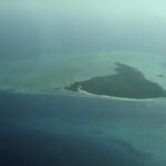Die Insel Misali aus dem Flugzeug, ein Dreieck aus Wald mit weißem Strand, auf einem türkisen Riffdach inmitten dunkelblauen Meeres, im Dunst