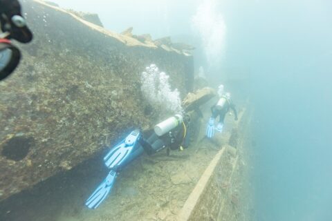 Zwei Taucher schwimmen auf dem Deck der Thistlegorm einen Gang entlang, in milchig blauem Wasser