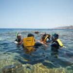 Schwimmer mit gelben Westen, Masken und Schnorcheln im klaren Wasser des Blue Hole, dahinter die Berge des Sinai